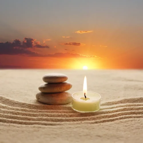 A candle and a rock resting on the sand with a sunset, creating a reflective moment.